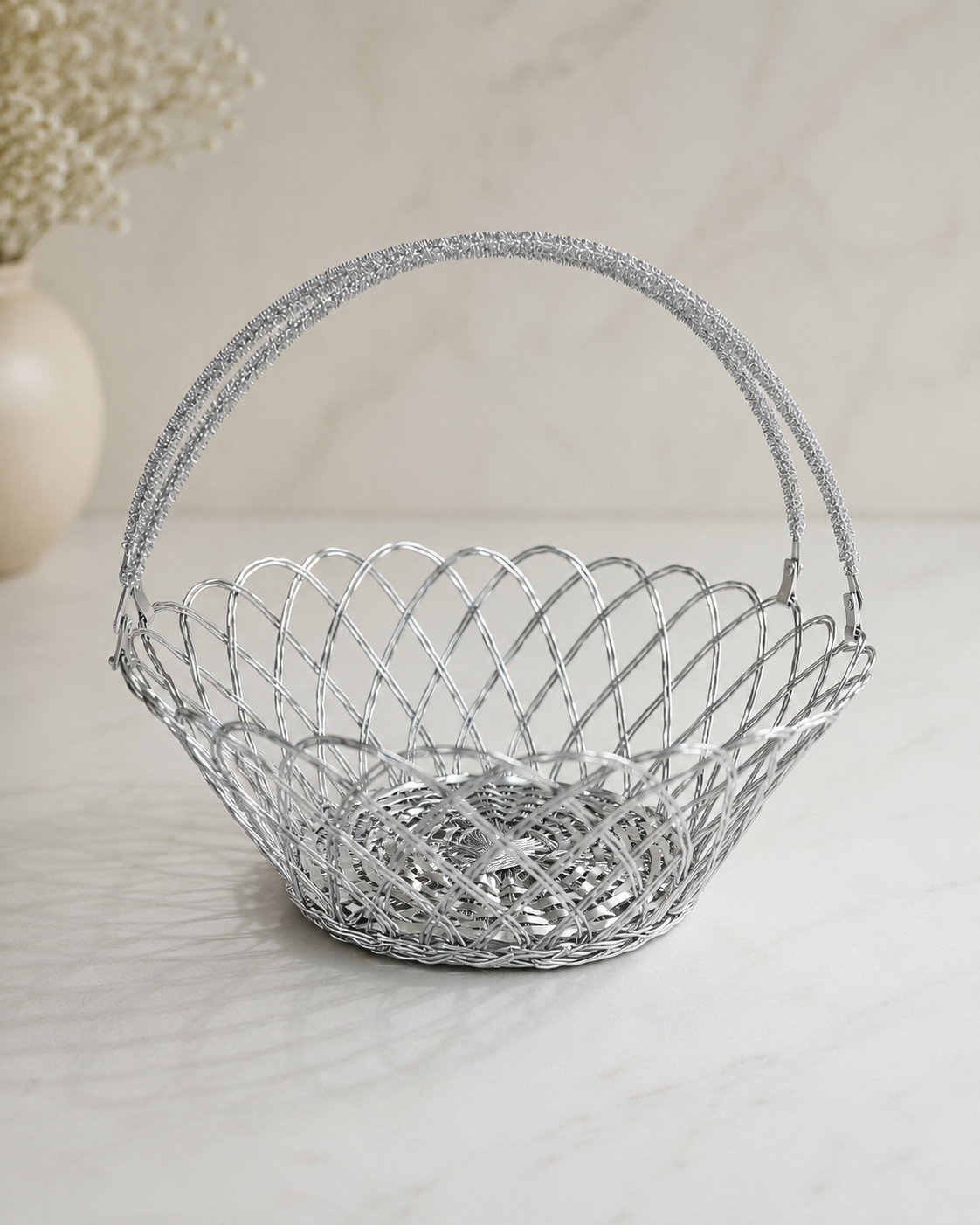 A silver flower-shaped wire tokra with an open woven design and arched handle, suitable for flowers, sweets, dry fruits, festive gifts, and return favours.