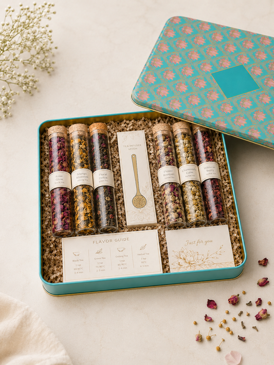 A turquoise printed tin gift box with six assorted loose leaf tea tubes, a tea infuser spoon, flavour guide, note card, and shredded paper packaging for elegant gifting.
