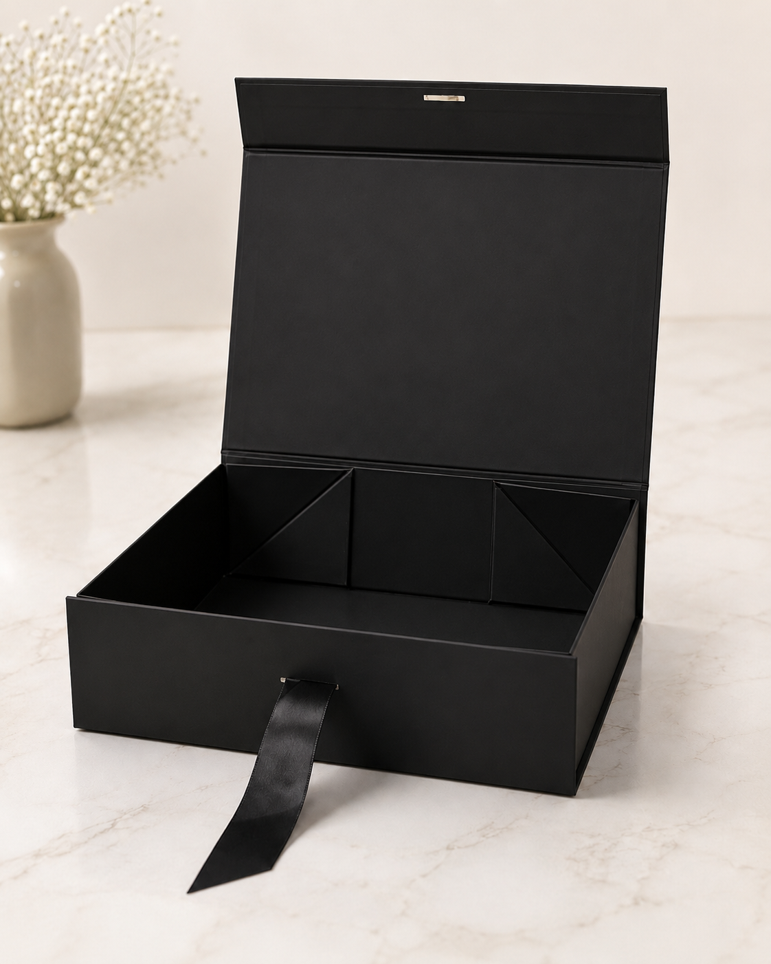 A black collapsible gift box with a hinged lid and ribbon pull, featuring a structured interior for organising curated gifts, corporate hampers, and festive packaging.