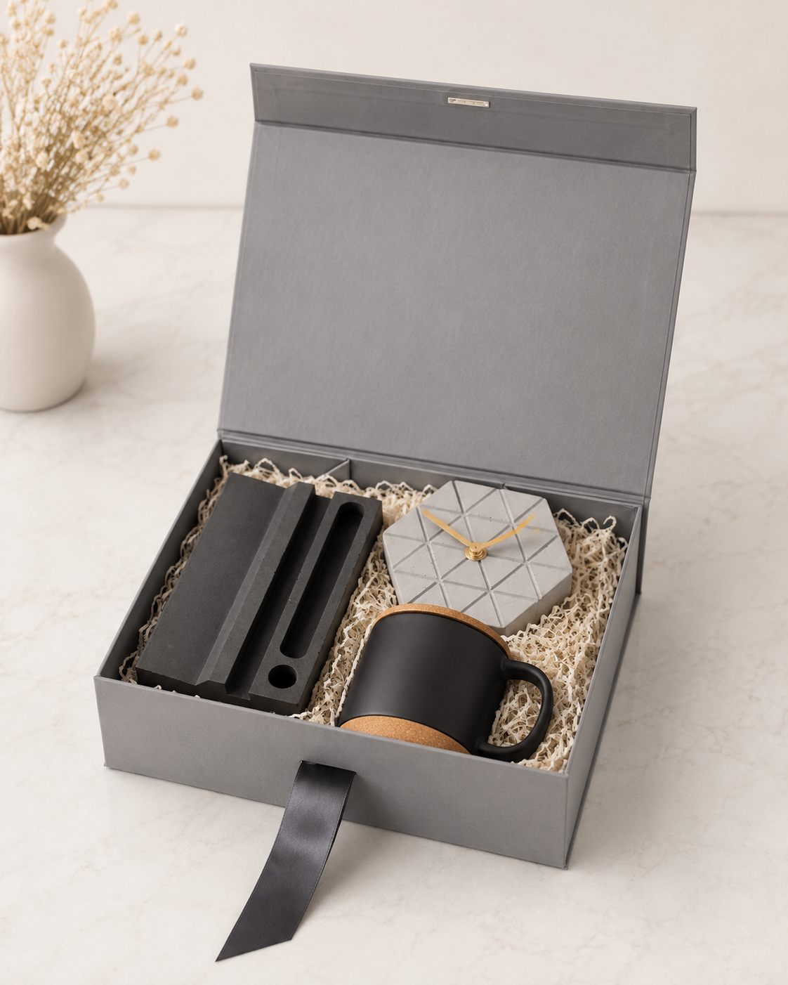 A premium grey collapsible gift box featuring a desk organizer, hexagon concrete desk clock, black cork mug, and shredded paper packaging for elegant corporate gifting.