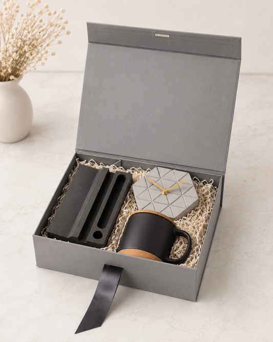 A premium grey collapsible gift box featuring a desk organizer, hexagon concrete desk clock, black cork mug, and shredded paper packaging for elegant corporate gifting.