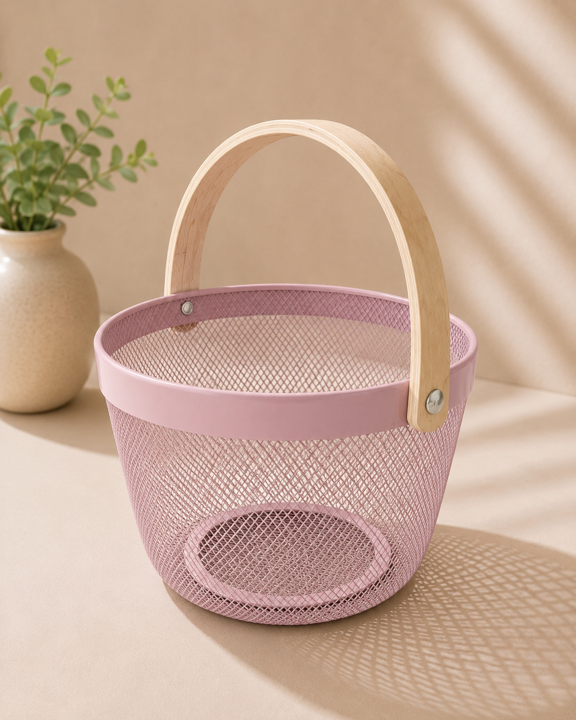 A pink round metal gift basket with a fine perforated texture and arched handle, suitable for bridal shower hampers, beauty products, candles, flowers, chocolates, and small gifts.