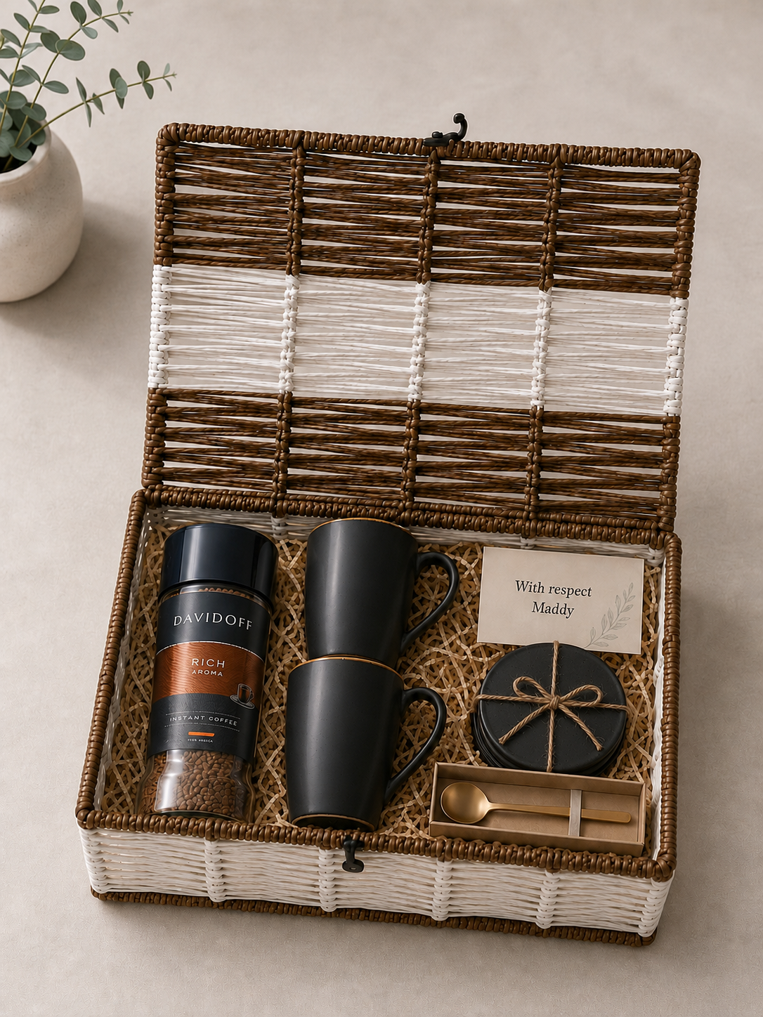 A reusable white and brown trunk basket featuring Davidoff Rich Aroma coffee, two matte black mugs, black coasters, a gold spoon, a message card, and shredded paper packaging.
