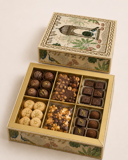 The Royal Indulgence Box featuring six compartments filled with assorted chocolate truffles, nutty chocolate clusters, brownie bites, cookies, caramel treats, popcorn, and chocolate squares in a decorative festive box.