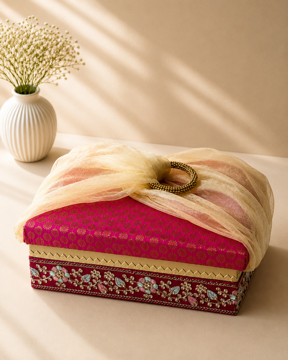 A decorative pink gift box with traditional printed detailing and gathered white net handles, suitable for saree gifting, bridal trousseau, sweets, dry fruits, chocolates, and wedding hampers.
