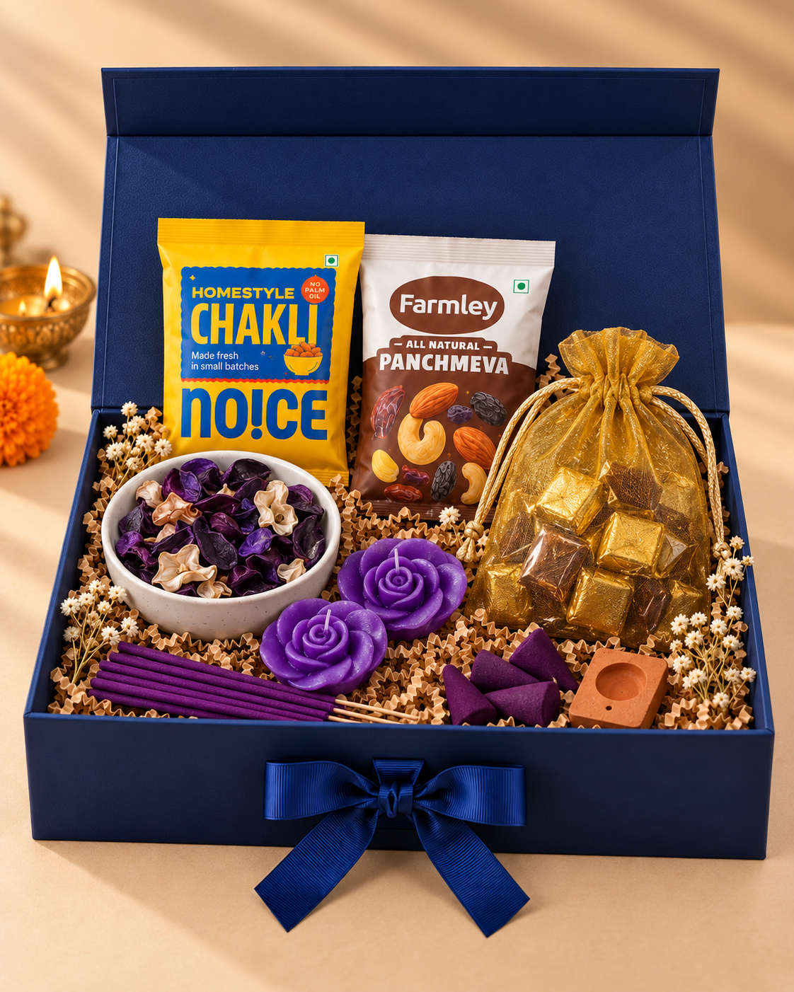 The Aroma Indulgence Hamper arranged in a premium navy magnetic ribbon box with assorted chocolates in a golden pot, Homestyle Chakli, Farmley Panchmeva, lavender fragrance items, potpourri, floating candles, incense sticks, incense cones, and an incense holder, finished with shredded paper.