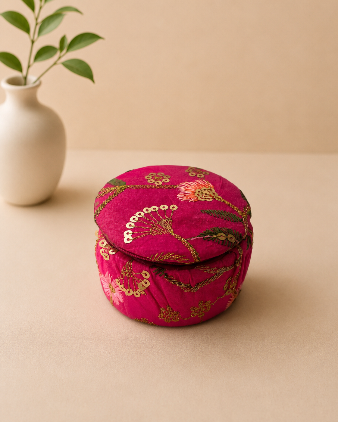 A small round fuchsia fabric dabbi with gold sequin embroidery and a fitted lid, ideal for presenting jewellery, chocolates, dry fruits, and festive keepsakes.