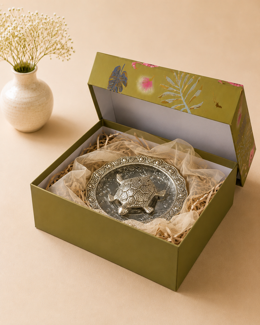 An olive green floral gift box featuring a German silver good luck turtle, styled with beige shredded paper and soft organza for elegant festive gifting.