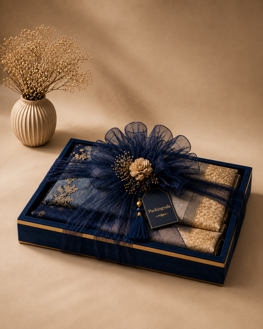 A premium blue saree gift box featuring a folded saree, decorative ribbon styling, floral embellishment, suede tray, and elegant ready-to-gift presentation.