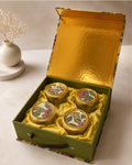 A floral designer gift box with a gold-finished interior, featuring four premium jars arranged in a satin-lined cavity for festive and corporate gifting.