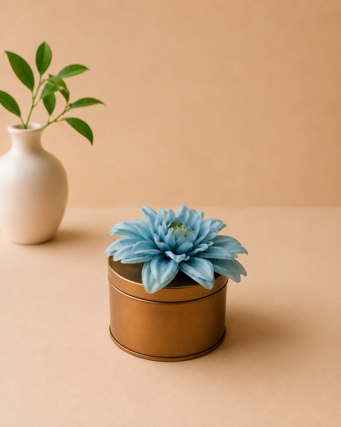 A small golden metal dabbi with a removable lid, decorated with a blue floral accent, suitable for gifting jewellery, chocolates, dry fruits, and festive keepsakes.