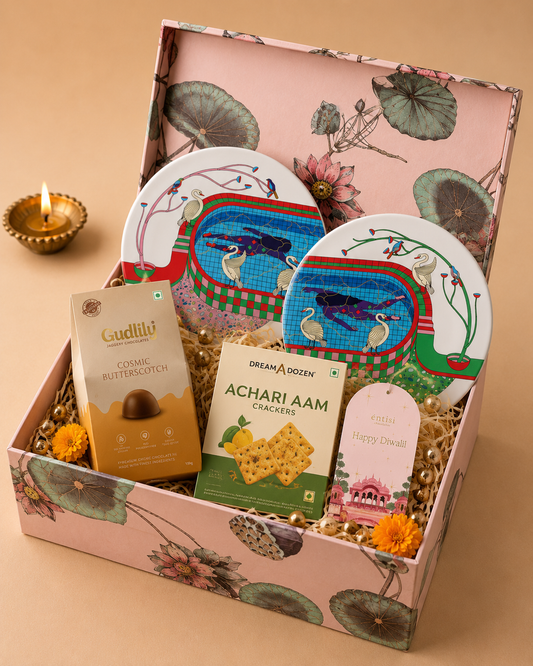 The Festive Table Hamper featuring decorative plates, achari aam crackers, jaggery chocolates, and a Diwali greeting card in a floral printed gift box.