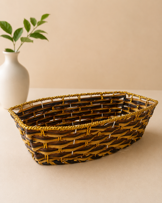 A brown and golden woven basket with an elongated open design, suitable for arranging dry fruits, sweets, chocolates, candles, and festive hamper essentials.
