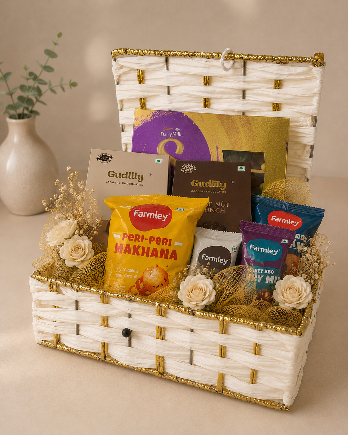 Golden Treats Trunk featuring Dairy Milk Silk, Gudlily chocolates, peri-peri makhana, Farmley snacks, and golden festive decoration in a reusable white woven trunk basket.