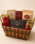 A rustic woven basket featuring a Rakhi, almond roasted tin, kaju katli box, premium dry fruit mix, chocolate almonds, kesar badam cookies, and festive floral styling for Raksha Bandhan gifting.