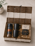 A reusable white and brown trunk basket featuring Davidoff Rich Aroma coffee, two matte black mugs, black coasters, a gold spoon, a message card, and shredded paper packaging.