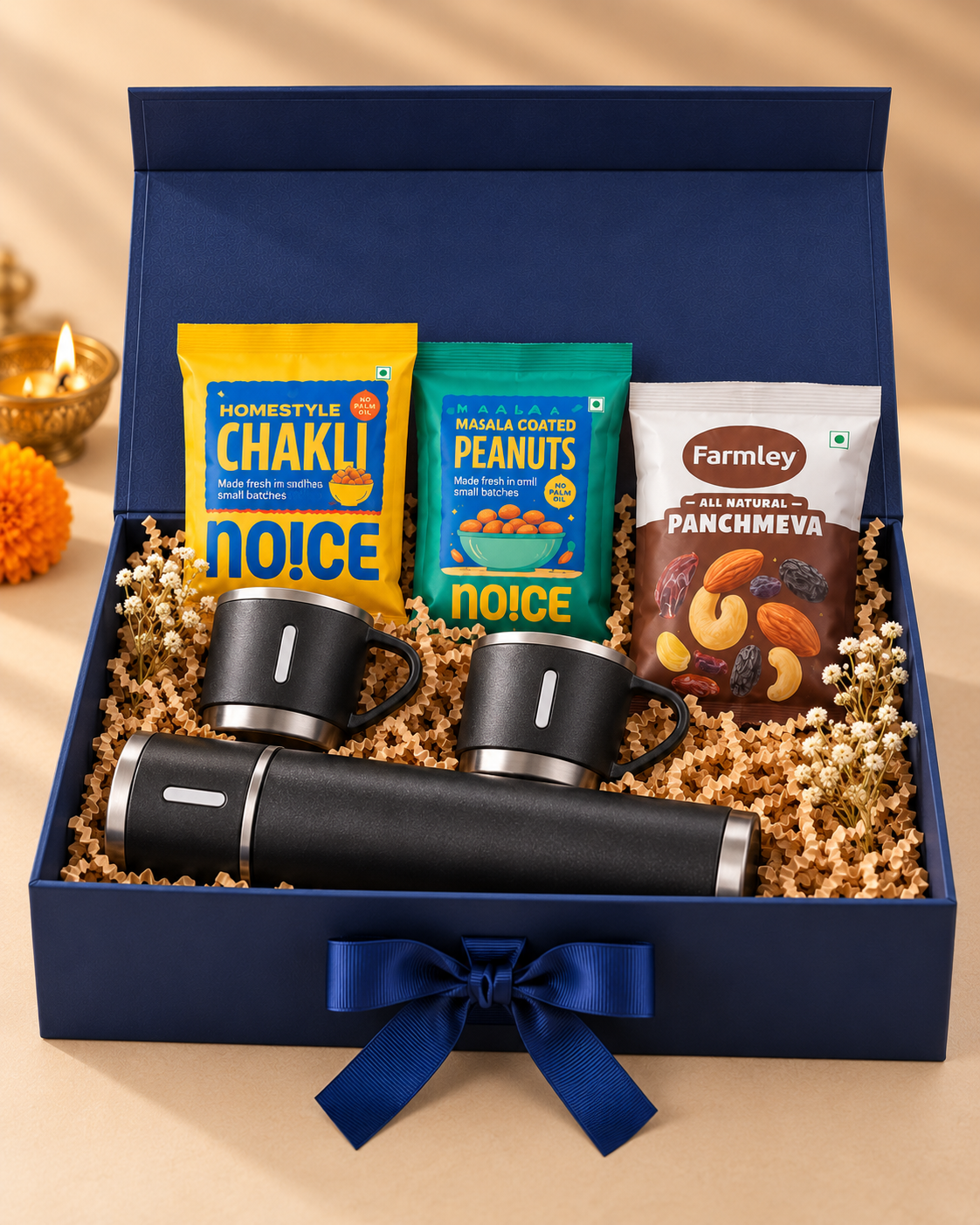 The Brew & Bites Gift Box arranged in a navy magnetic ribbon box with a vacuum flask, two mugs, chakli, salted peanuts, makhana, and panchmeva.